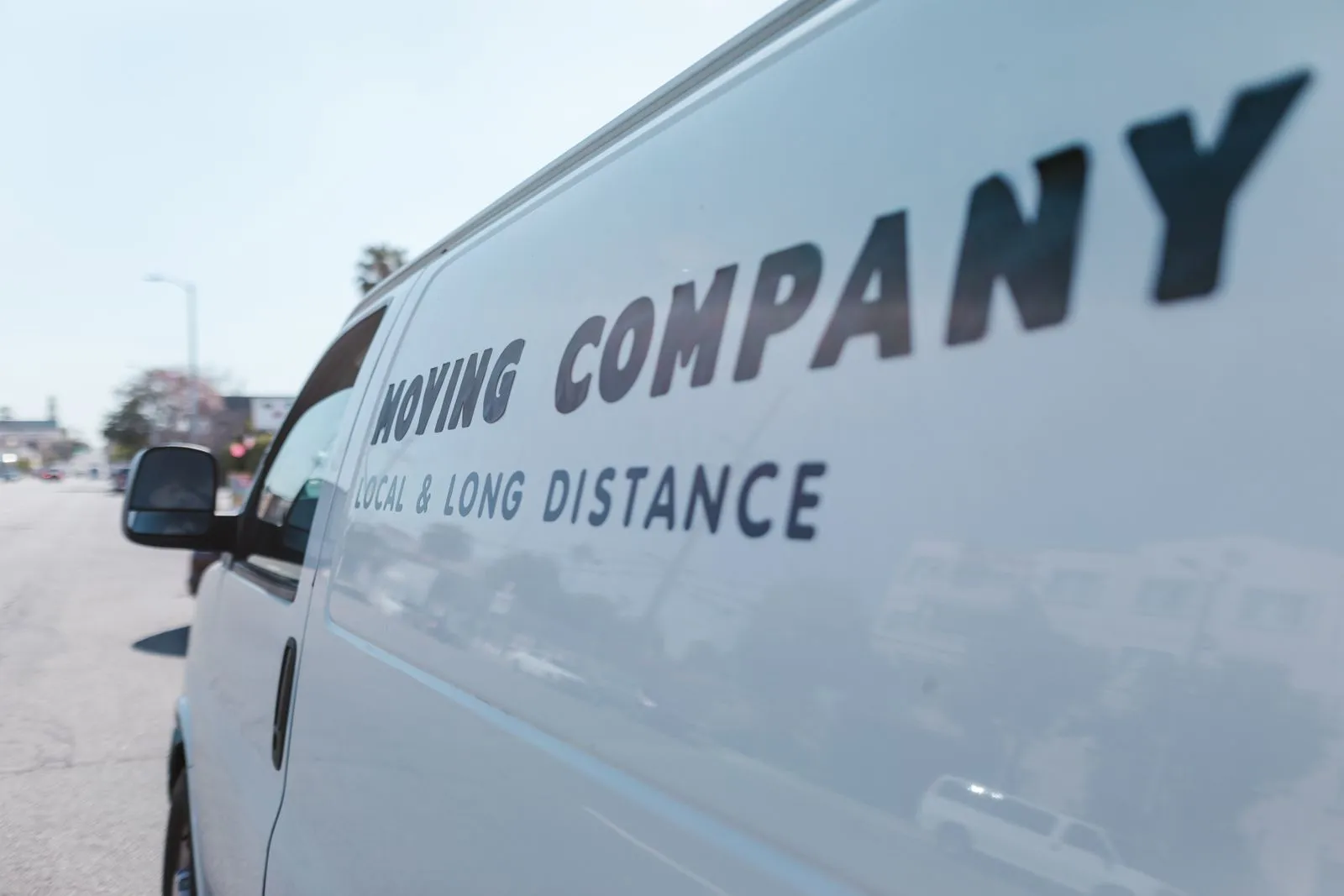 Close-up of a white moving company van with text on a sunny day street.